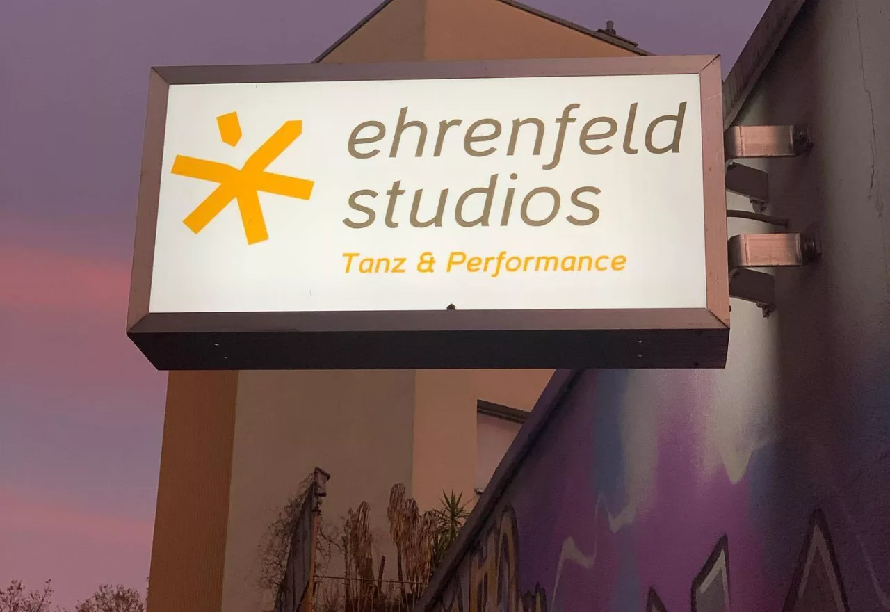 Das Foto zeigt das Leuchtschild der ehrenfeldstudios mit dem Schriftzug und einem orangem Stern vor einem rosa-lila Abendhimmel